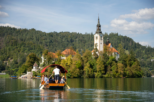 Image of Lake Bled in Slovenia taken from the bank showing a traditional wooden boat taking people to the island.