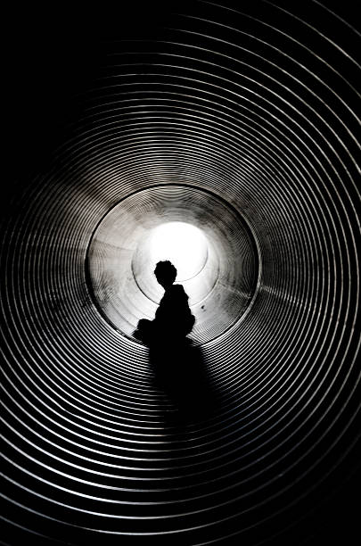 garçon assis silhouette avec la lumière au bout du tunnel - spirituality light tunnel light at the end of the tunnel photos et images de collection