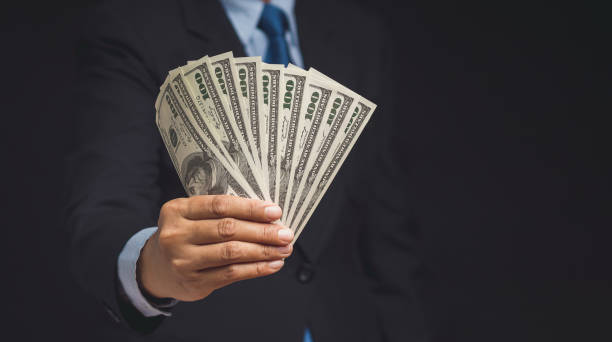 istock Businessman holding US dollar bills while standing on a black background 1770069764