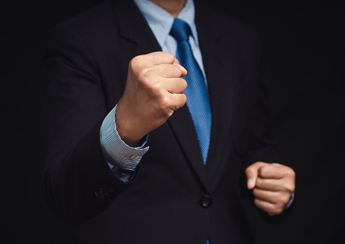 Businessman in a suit raised a fist while standing on a black background Fighting, victory, success, and winning concept. Close-up photo