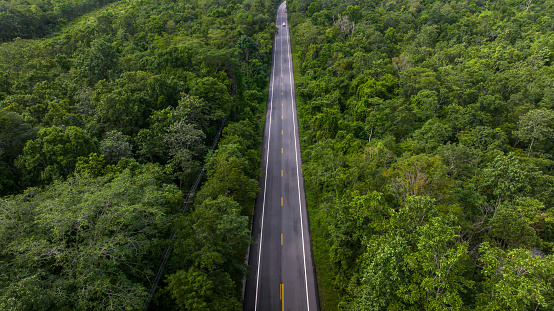 Aerial view over  forest road with asphalt road and forest, Road in the middle of the forest up to mountain, Countryside road passing through the green forrest and mountain.