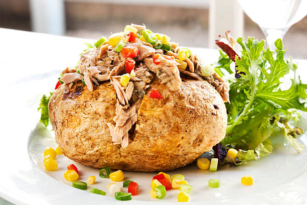 Serving of baked potato with tuna and vegetable filling Baked potato filled with tuna, corn, and capsicum.  Salad greens behind. baked potato stock pictures, royalty-free photos & images