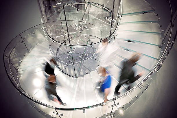 Business people in motion on transparent spiral staircase stock photo