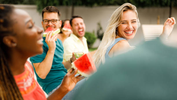 Carefree woman having fun on a party with her friends. Panoramic view of cheerful woman having fun with her friends on a party in the backyard. black man eating watermelon stock pictures, royalty-free photos & images
