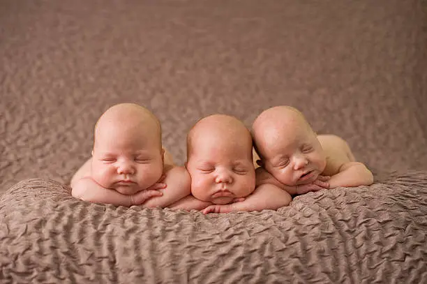 3 identical triplet girls sleeping peacefully on a soft blanket.