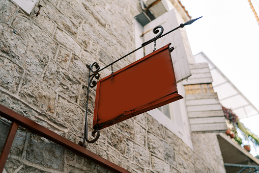 Empty tablet hangs on a forged signpost on the stone facade of an old house. High quality photo
