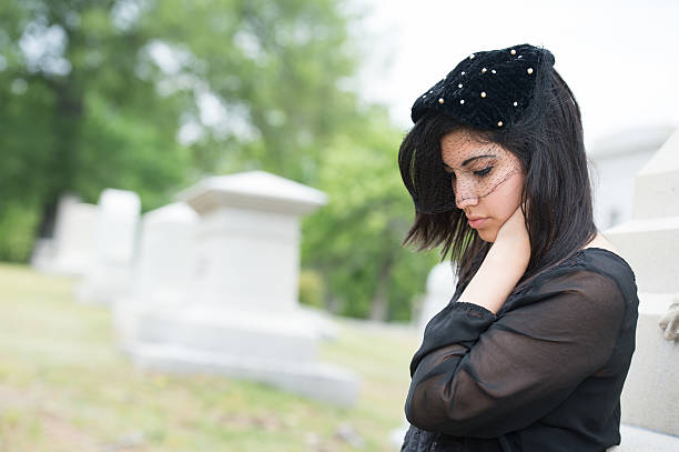 Solitary woman mourning with her hand on headstone, remembering dead relatives in on Pere Lachaise cemetery in Paris, France.