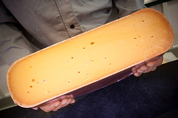 Man holding a big Gouda Cheese Man in store holding a big Gouda Cheese cut in half cheese dutch culture cheese making people stock pictures, royalty-free photos & images