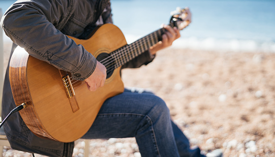 Musician plays the acoustic guitar while sitting on a chair on the beach. Cropped. Faceless. High quality photo