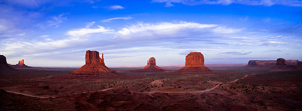 Monument Valley Panorama "Panorama of Monument Valley at dusk, with the shadow of the East Mitten draping the West Mitten.  This phenomena occurs only twice a year.  This Navajo Tribal Park is the iconic western landscape portayed in movies over the decades. A dirt road can be seen in the foreground." west mitten stock pictures, royalty-free photos & images