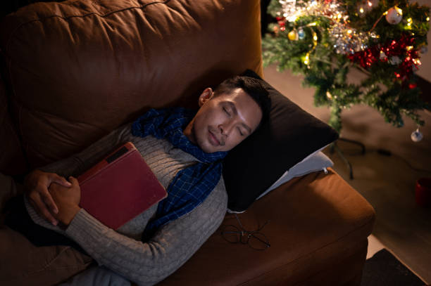 istock A tired Asian man falls asleep while reading a book, sleeping on a sofa in the living room. 1770176835