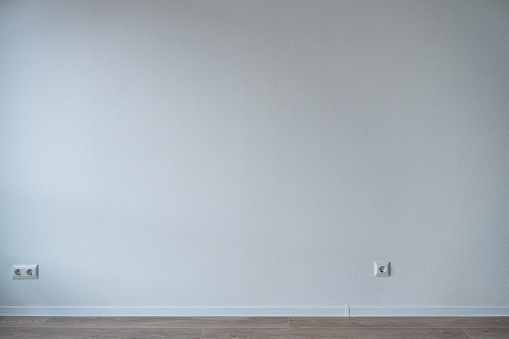 Abstract background, empty room interior, focus on the white wall with a white baseboard and an electrical outlet