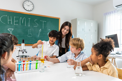 Adorable student learn with teacher in classroom at elementary school. Young brilliant and smart children sit on table and study chemistry experiment with happiness and fun activity at kindergarten.