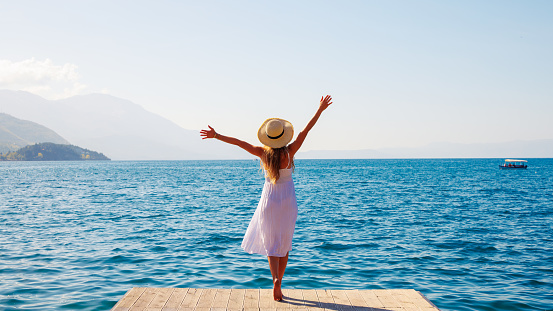 Happy woman in white dress standing on wooden pier enjoying beautiful lake- Ohrid in Macedonia