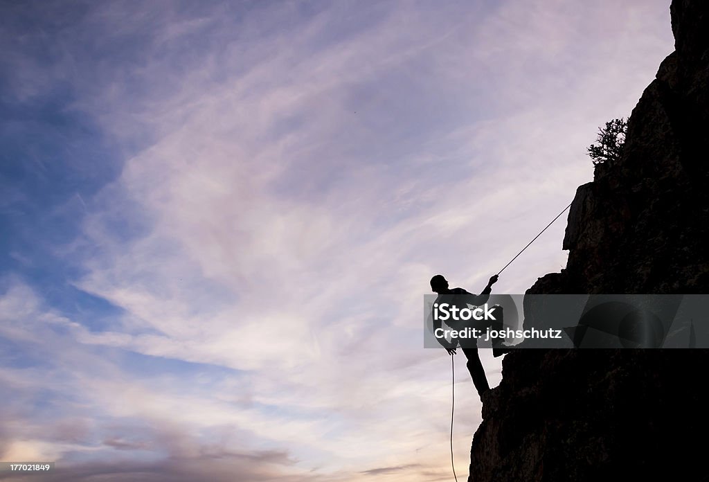 Rappeling A man rappels down a mountain face during sunset Colorado Stock Photo