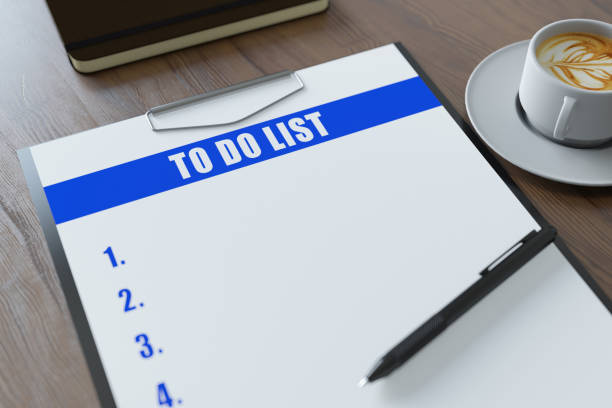 A white piece of paper with the words To Do written on it. The paper is open to a blank page with a list of tasks written on it. The paper is on a wooden surface