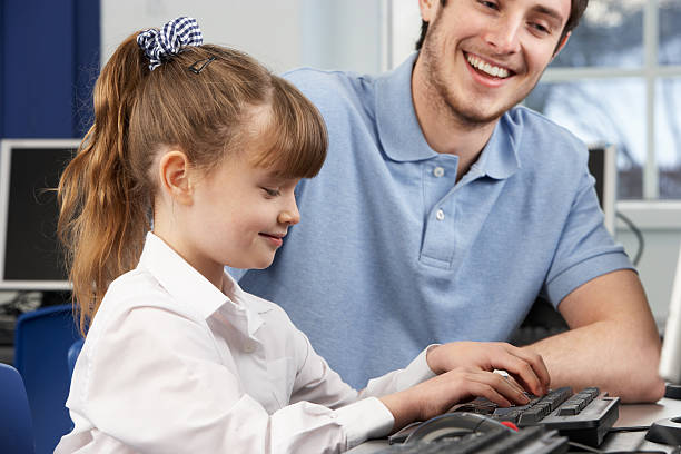 Teacher helping girl using computer in class stock photo