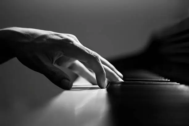 "A black and white image of an adult male hand rested on a piano.  The image is sharp and detailed, with a very shallow depth of field."