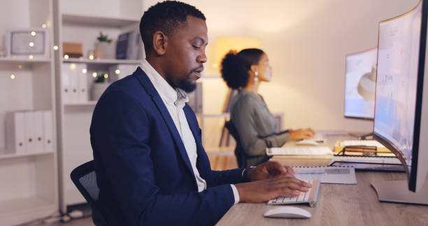 istock Business, night and black man typing on computer in office working late for planning, proposal and project. Corporate, focus and male worker at desk for writing email, website research and report 1770256841