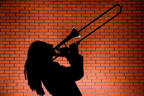 Man playing trombone in front of a red brick wall
