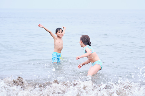 A boy and a girl are having fun playing in the sea in the waves.