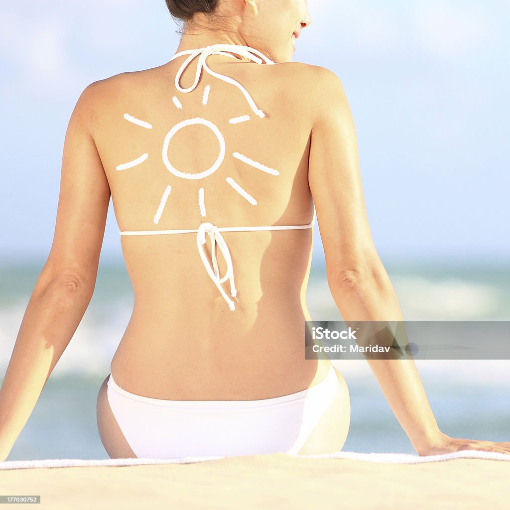 Sunscreen / sun tan lotion Sunscreen / sun tan lotion sun drawing on xwoman back. Girl in bikini sitting on beach in sunlight. Illustration Stock Photo