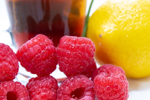 A cup of steaming hot tea surrounded by ripe raspberries and freshly cut lemons