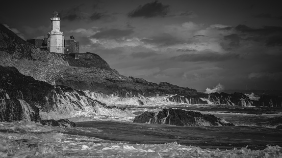 Experience the timeless drama of nature in this striking black and white photograph capturing Mumbles Lighthouse amidst a fierce storm. Waves crash against the rocks, leaving behind a trail of white foam streaming down the rugged surface. The monochrome palette enhances the mood, emphasizing the power and intensity of the moment. This evocative composition perfectly captures the raw energy of the sea, making it an ideal choice for projects seeking a dramatic and atmospheric backdrop.