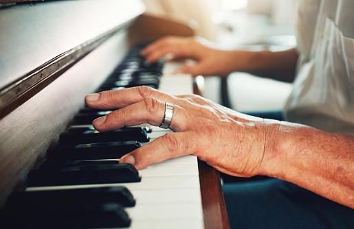 Hands, piano and senior man playing for music in living room for musical entertainment practice. Instrument, hobby and elderly male person in retirement enjoying a song on keyboard at modern home.
