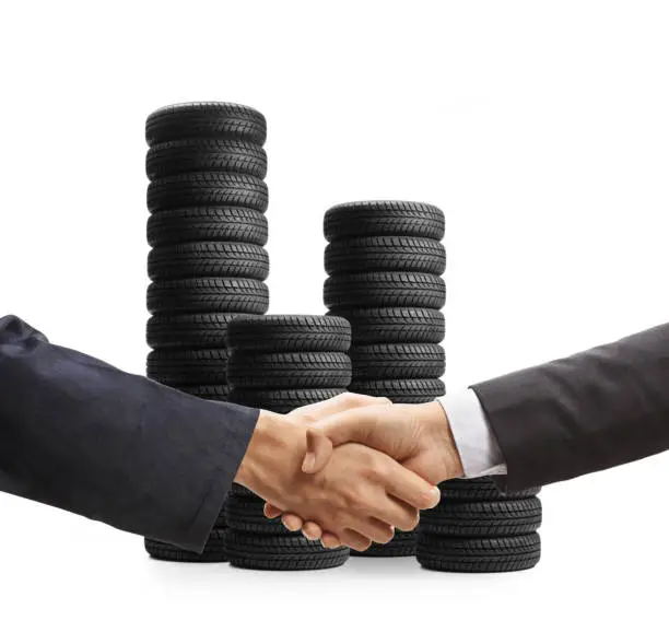Auto mechanic and a businessman shaking hands in front of car tires isolated on white background