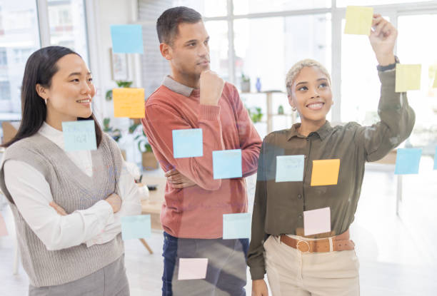 istock Creative people, planning and thinking for schedule, team strategy or brainstorming on glass wall at office. Group in teamwork contemplating plan, tasks and post it for sticky note or startup 1770344448
