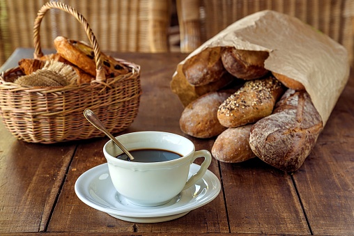 White cup of espresso, wicker basket with traditional french viennoserie and breads on old wooden background