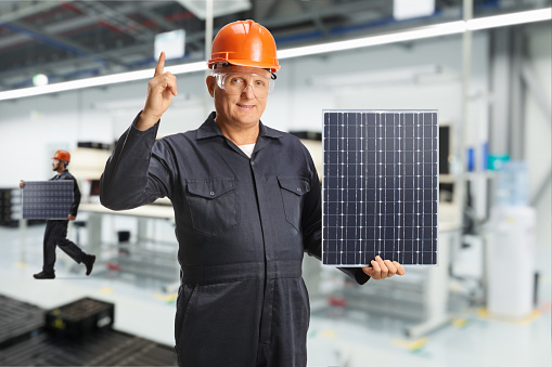 Workers inside a factory holding a solar panel and pointing