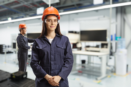 Young female technician with a helmet and goggles at a solar panel production line
