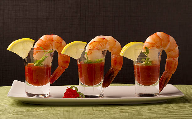 Prawn Cocktail A trio of prawns each hanging on a shot glass filled with cocktail sauce and garnished with a lemon wedge and pea shoots.  On a white plate on top of a light green placemat against a dark textured background. shrimp cocktail stock pictures, royalty-free photos & images