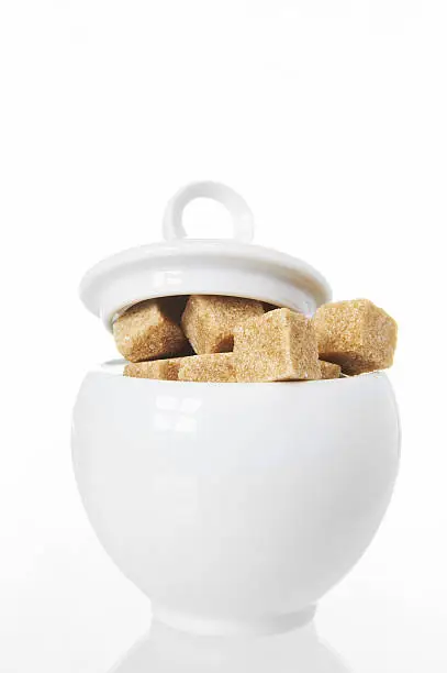 white sugarbowl with brown sugarcubes on white background