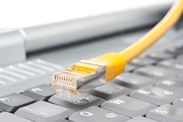 Macro of a yellow network cable in front of a computer keyboard