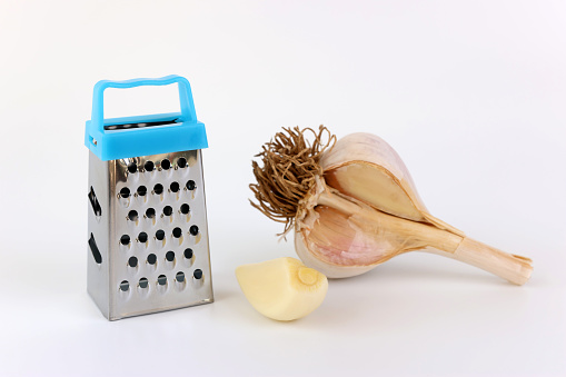 Hand held miniature grater and garlic on a white background.