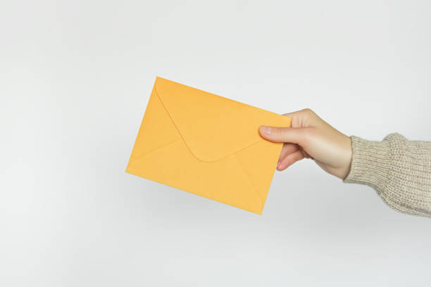 istock female hand holding a yellow envelope on a gray background 1770400659
