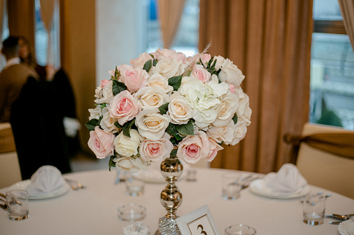 Close up of bridal bouquet of pink and white peony roses and greenery in glass vase on table outdoors, copy space. Wedding concept