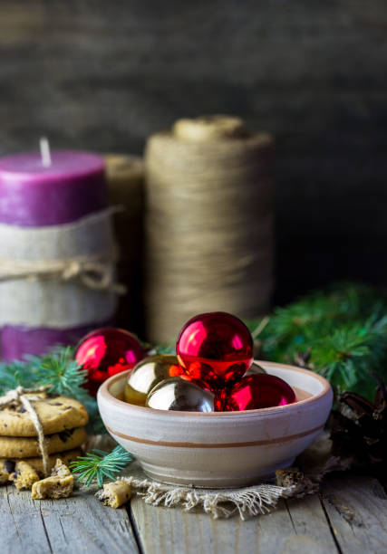 Christmas (New Year) decoration composition. Fur-tree branches, candle, twine, red glass balls in a plate, baked chocolate chip cookies on wooden background