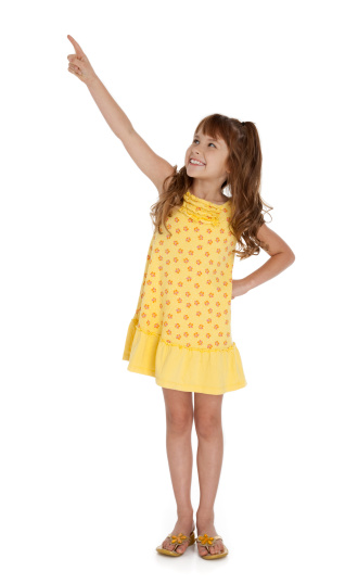 Full length photo of little wearing yellow summer dress pointing upward, on white background.