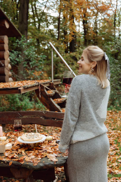 la jeune fille profite de la nature automnale. boit du vin rouge en regardant la forêt autour - autumn table setting flower photos et images de collection
