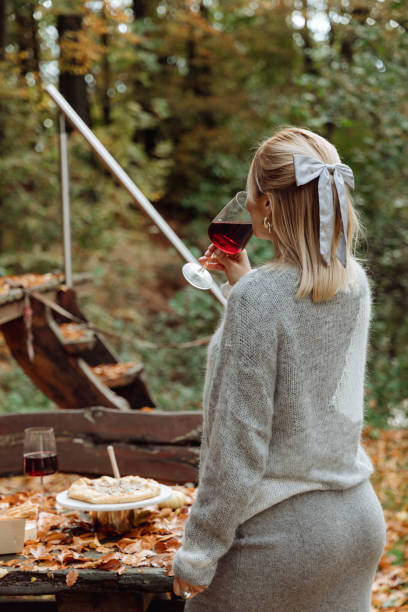 la jeune fille profite de la nature automnale. boit du vin rouge en regardant la forêt autour - autumn table setting flower photos et images de collection