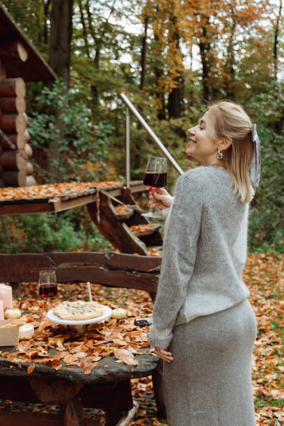 la jeune fille profite de la nature automnale. boit du vin rouge en regardant la forêt autour - autumn table setting flower photos et images de collection