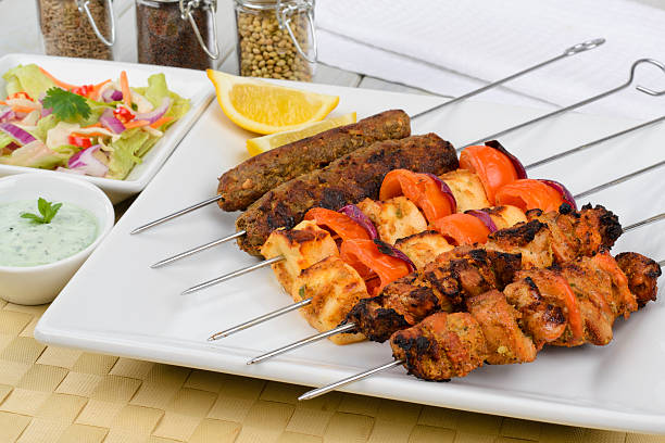 Six kebab skewers laid out on white square plate
