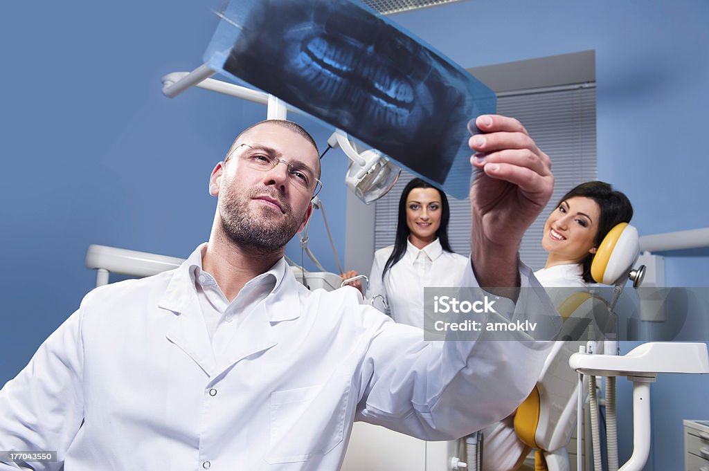 At dental clinic Dentist with x-ray and smiling patient and assistant in the background Adult Stock Photo