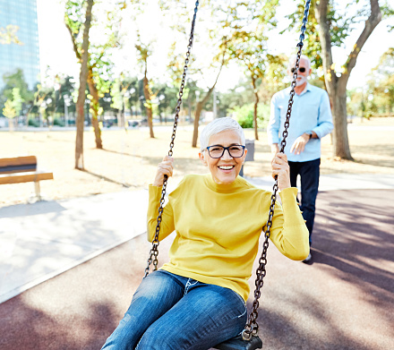 Happy active senior couple having fun on a swing in park outdoors