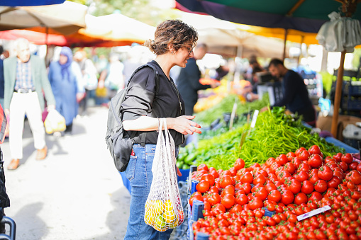 Woman with net in hand shopping for fruits and vegetables at farmers market