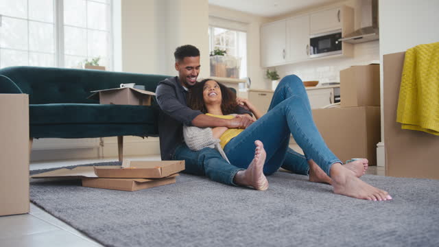 Couple Looking Around New Home Celebrating Sitting On Floor Eating Takeaway Pizza On Moving Day